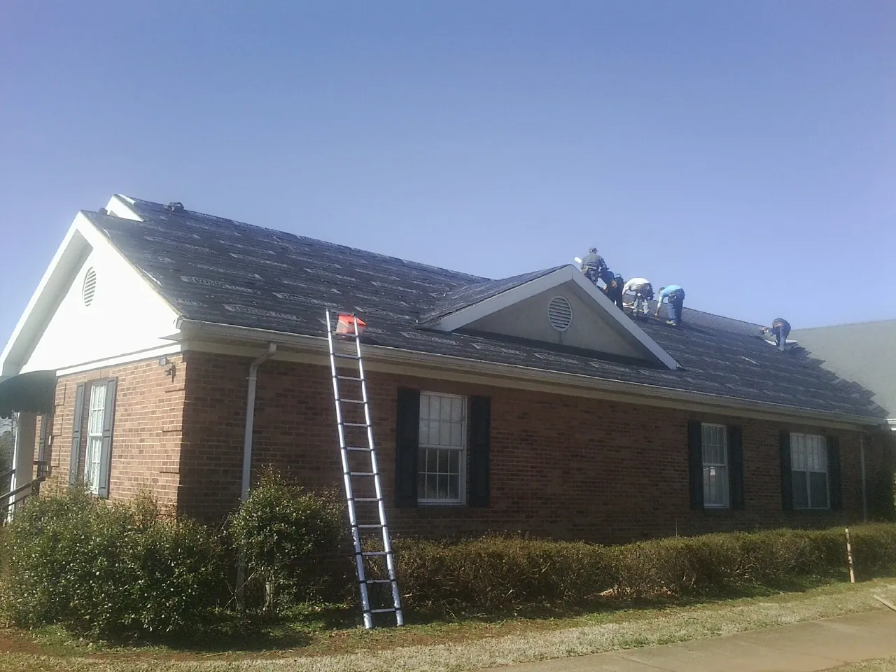 Crew tearing shingles off a brick ranch roof with a ladder set — Metal Roof Repair work by our crew in Sycamore