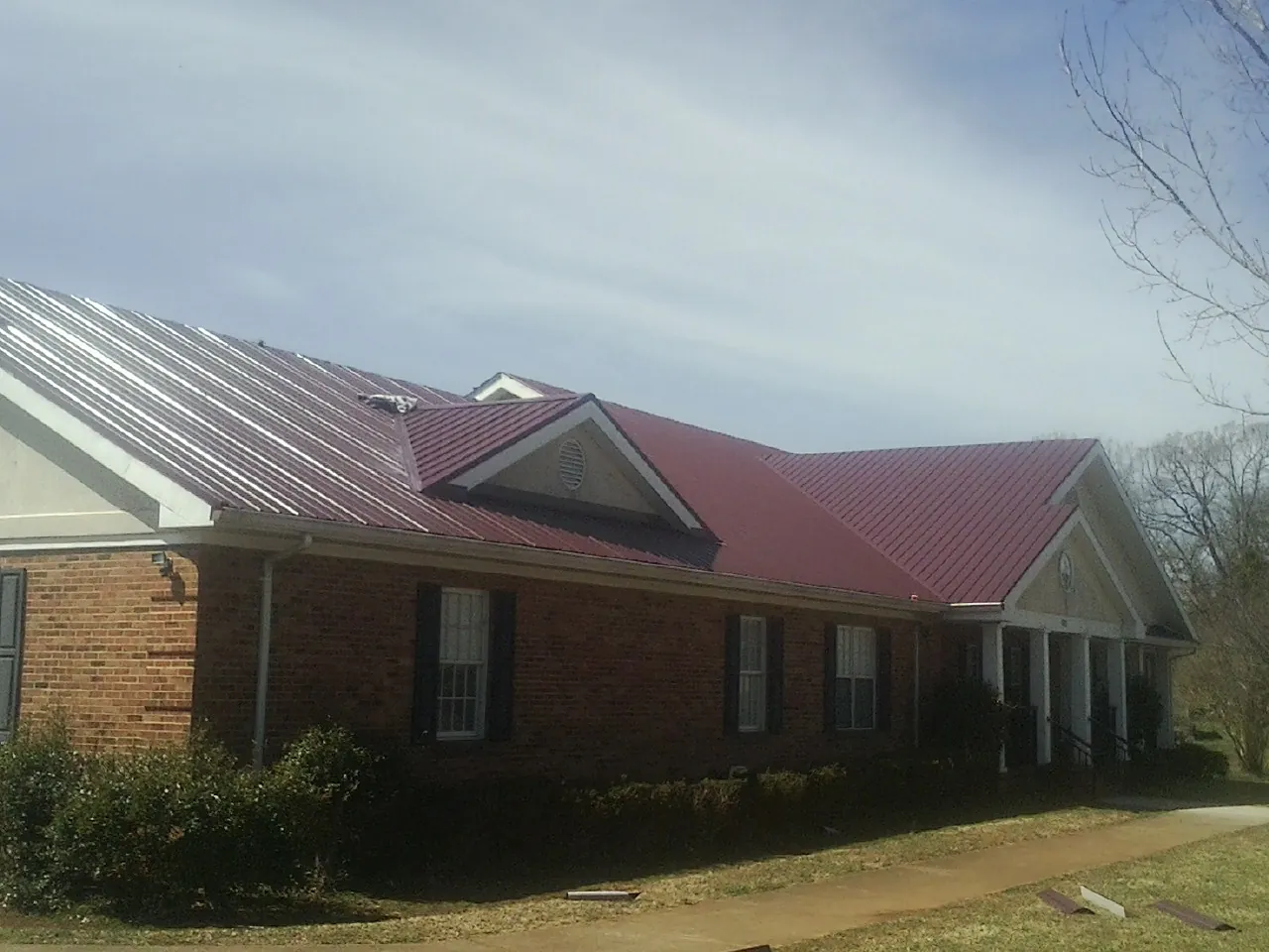 Red metal roof with gabled entries on a long brick building, from a Hail Damage Roof Repair job in Sycamore